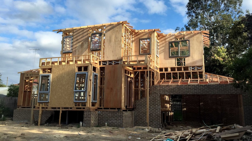 Construction site with large wooden and brick townhouse structure, with trees and blue sky in background