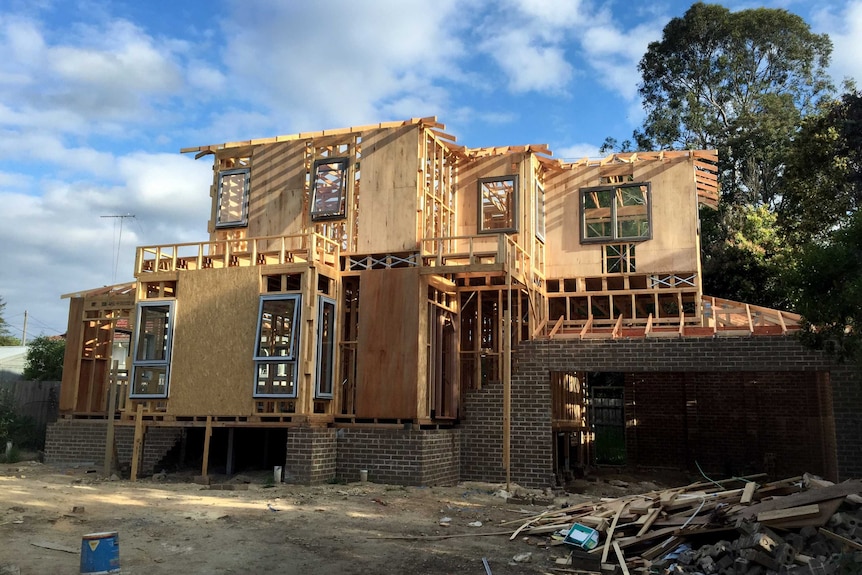 Construction site with large wooden and brick townhouse structure, with trees and blue sky in background