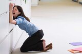 A businesswoman in a blue shirt leaning on a filing cabinet while crying.