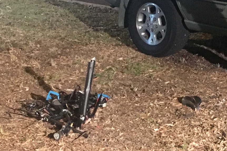 A close-up shot of the mangled wreckage of a bike frame on a road verge with the wheel of a four-wheel drive parked nearby.