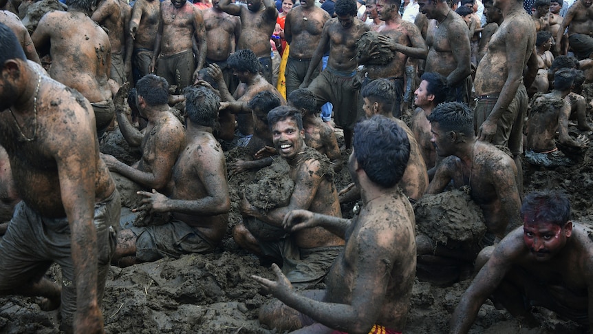 Shirtless men fling dung at each other in a pile of dung.