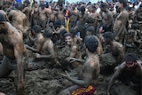 Shirtless men fling dung at each other in a pile of dung.