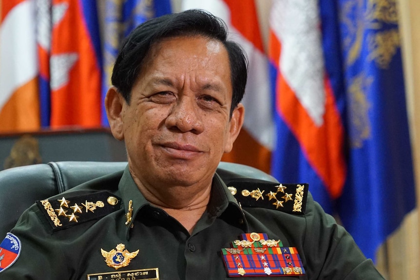 A Cambodian man in a naval uniform sits in a leather chair