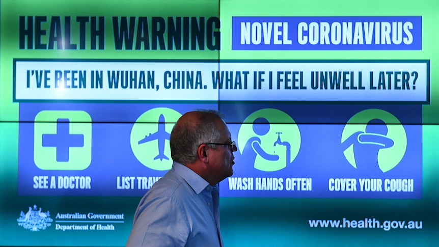Scott Morrison standing in front a large infograph about coronovirus