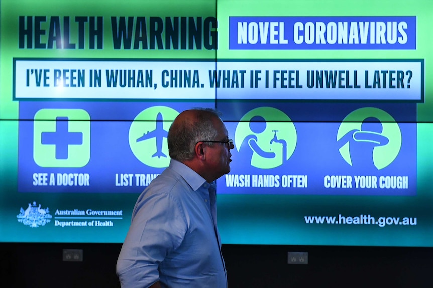 Scott Morrison standing in front a large infograph about coronovirus