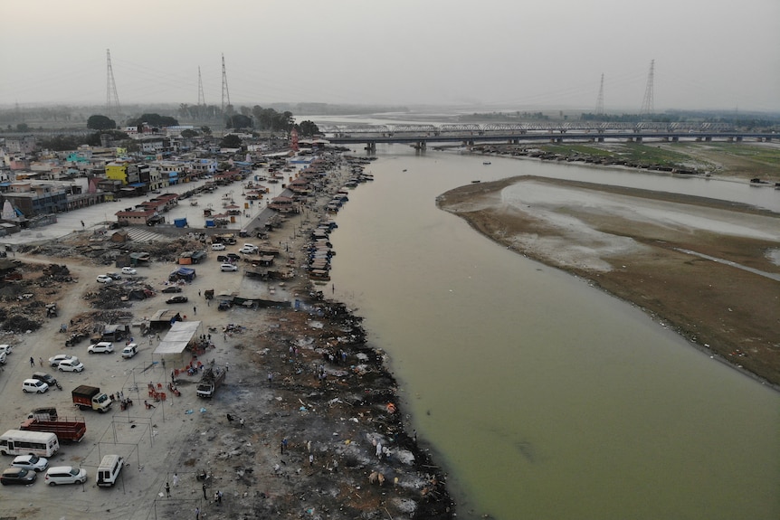 A river bank is black and grey with ash. The angle of the image shows the ashy bank stretching for miles.