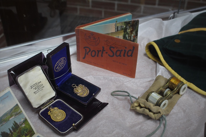 Medals, opera binoculars and an autograph book sit in a glass container on display 