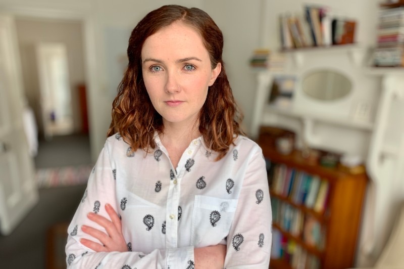 A woman with reddish hair looking at the camera with arms folded.