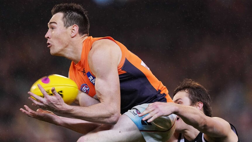 An AFL player takes an aerial mark on his chest as a defender reaches out behind him.