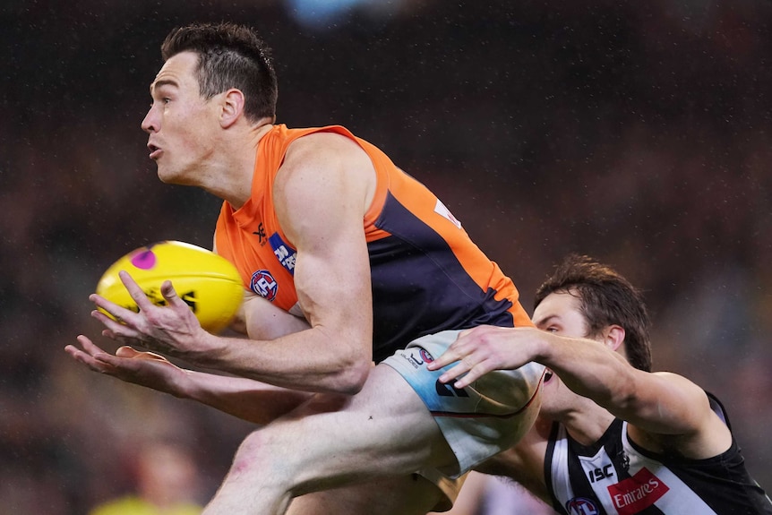 An AFL player takes an aerial mark on his chest as a defender reaches out behind him.
