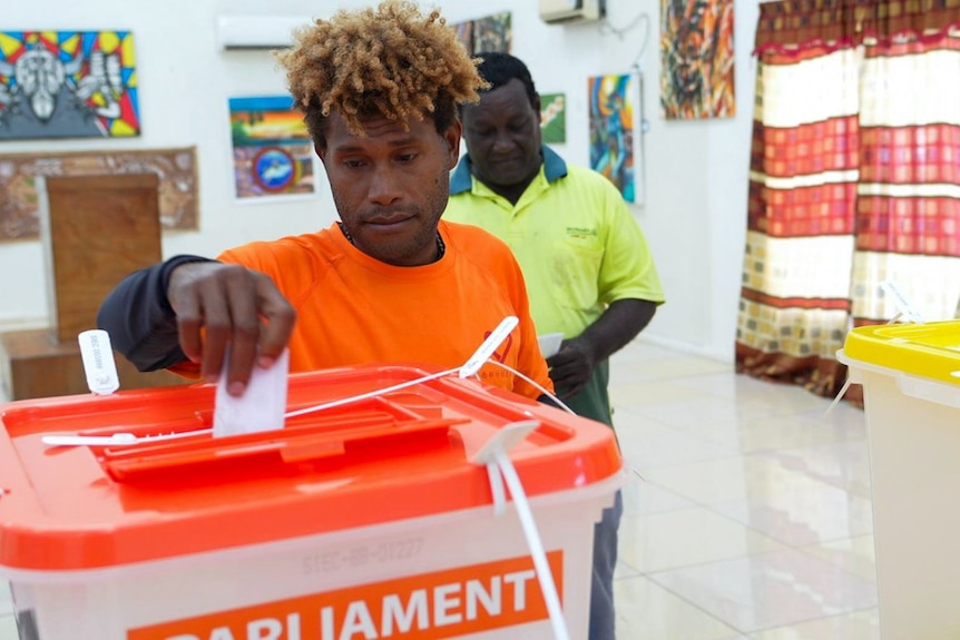 A Solomon Islander in a red shirt dropping a vote in a box
