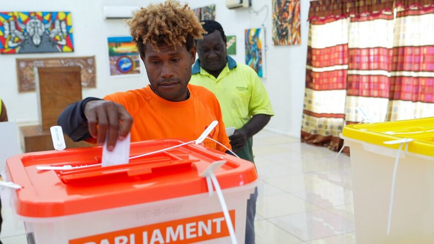 A Solomon Islander in a red shirt dropping a vote in a box