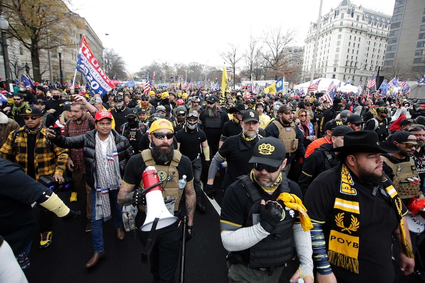 A large group of people dressed in yellow and black clothing walk on a street.