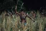 Black Woman staunchly running into battle through long gross. She is wielding asword dressed in stretch-knit top.
