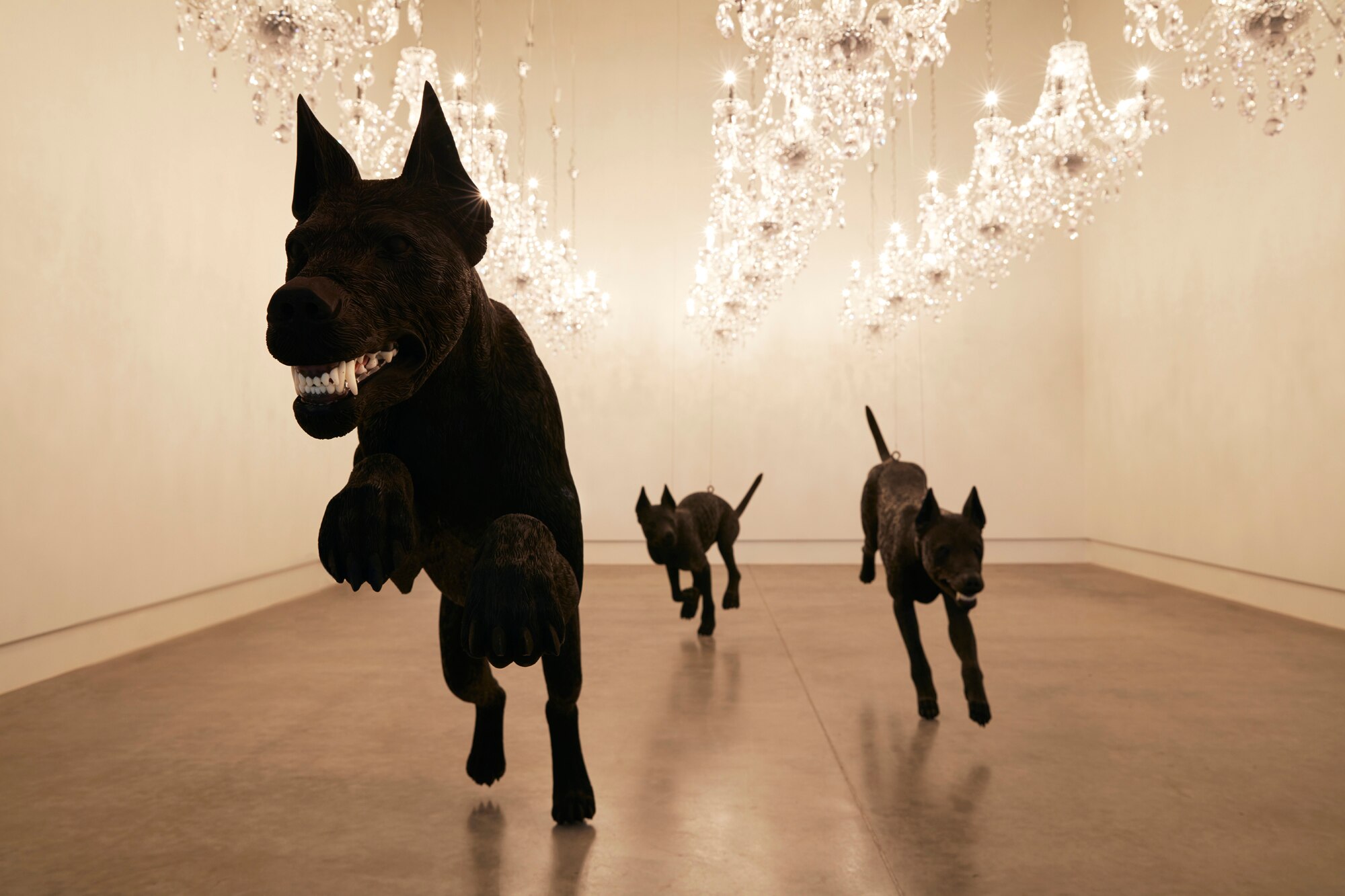 Three black, wooden dogs with bared fangs are posed mid-chase under a ceiling full of glittering crystal chandeliers.