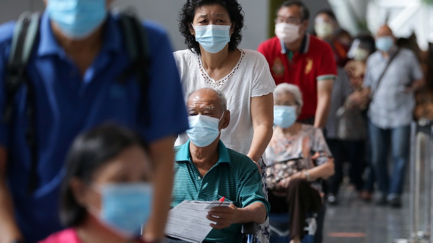 A line of people being pushed in wheelchairs, with everyone wearing masks.