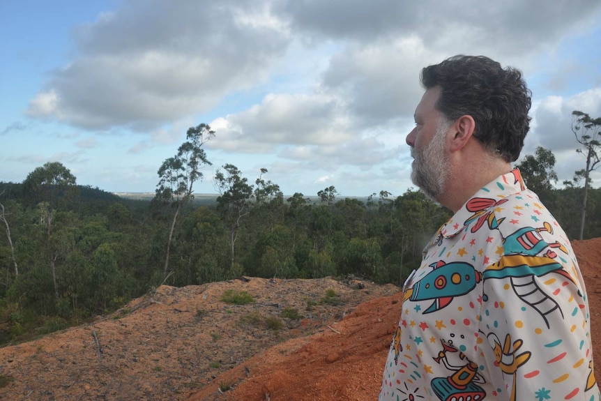 A NASA scientist looks out over a rocky outcrop and forest.