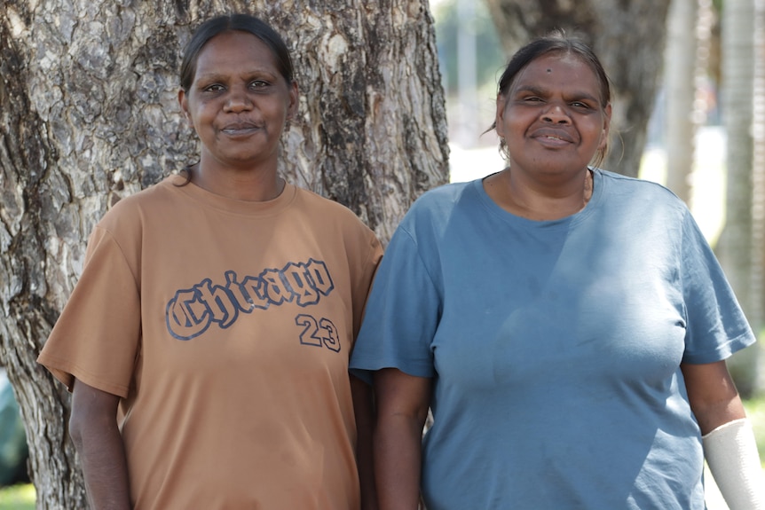 Two young Aboriginal woman stand in front of a tree