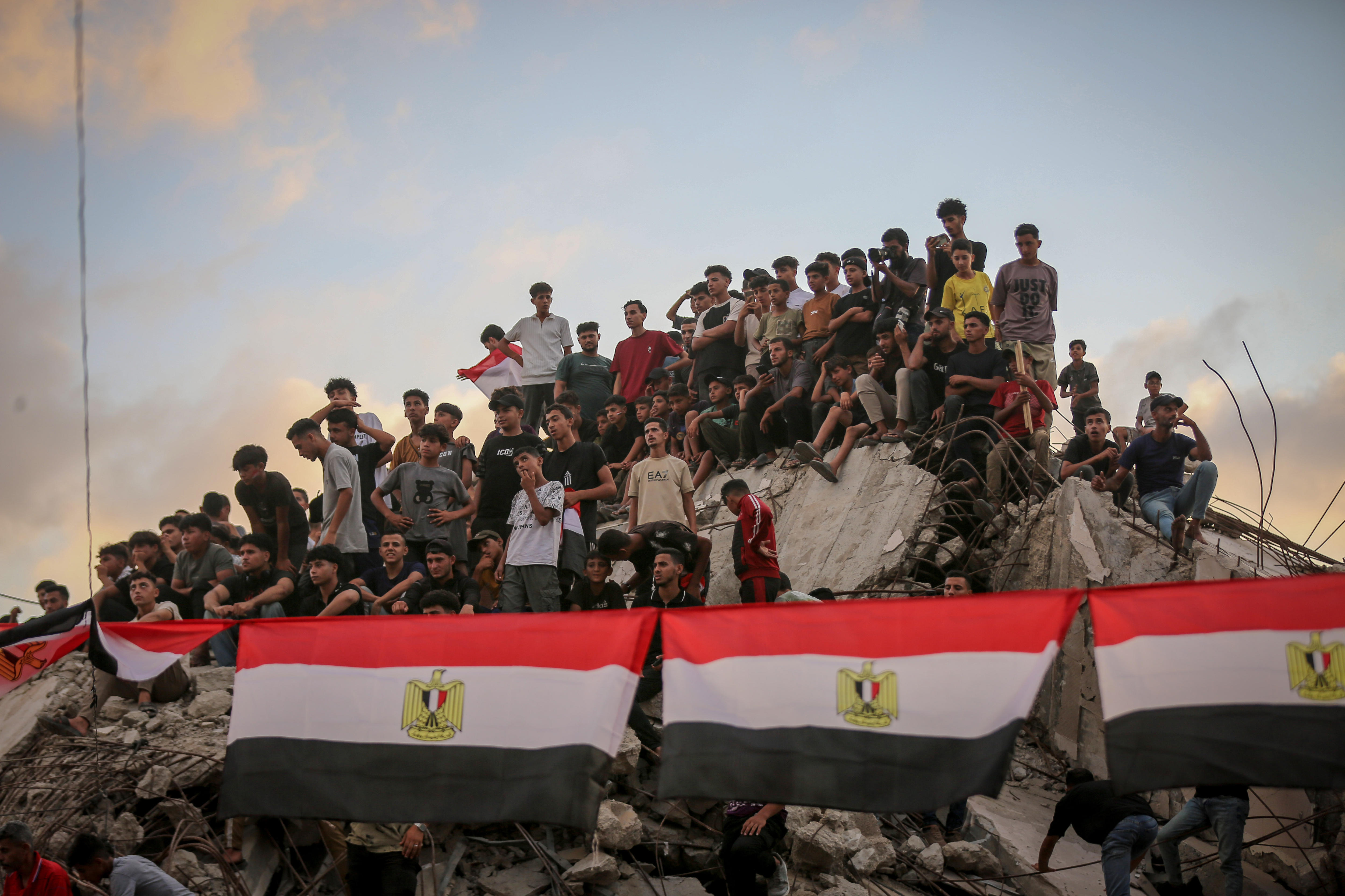 Palestinians sit on the rubble of a destroyed building, Egypt flags in the foreground