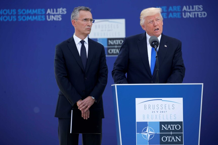 Donald Trump delivers a speech from a lectern with Jens Stoltenberg standing next to him.