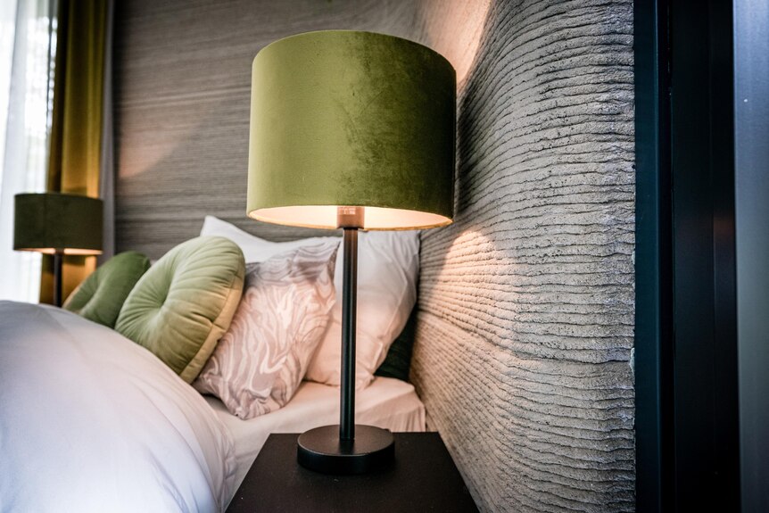 A lamp with a green shade illuminates a wall made of small, stacked horizontal concrete layers.