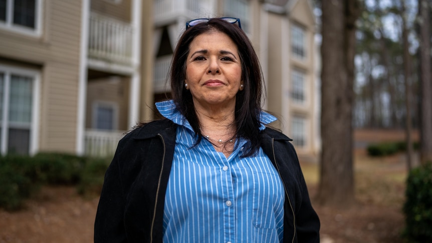 A woman in a blue oxford shirt and black jacket with a slight smile on her face 