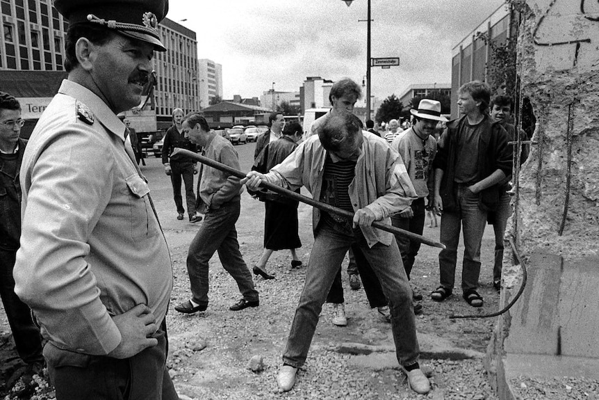 An East German border soldier watches a man hammering a section of the Berlin Wall near Checkpoint Charlie.