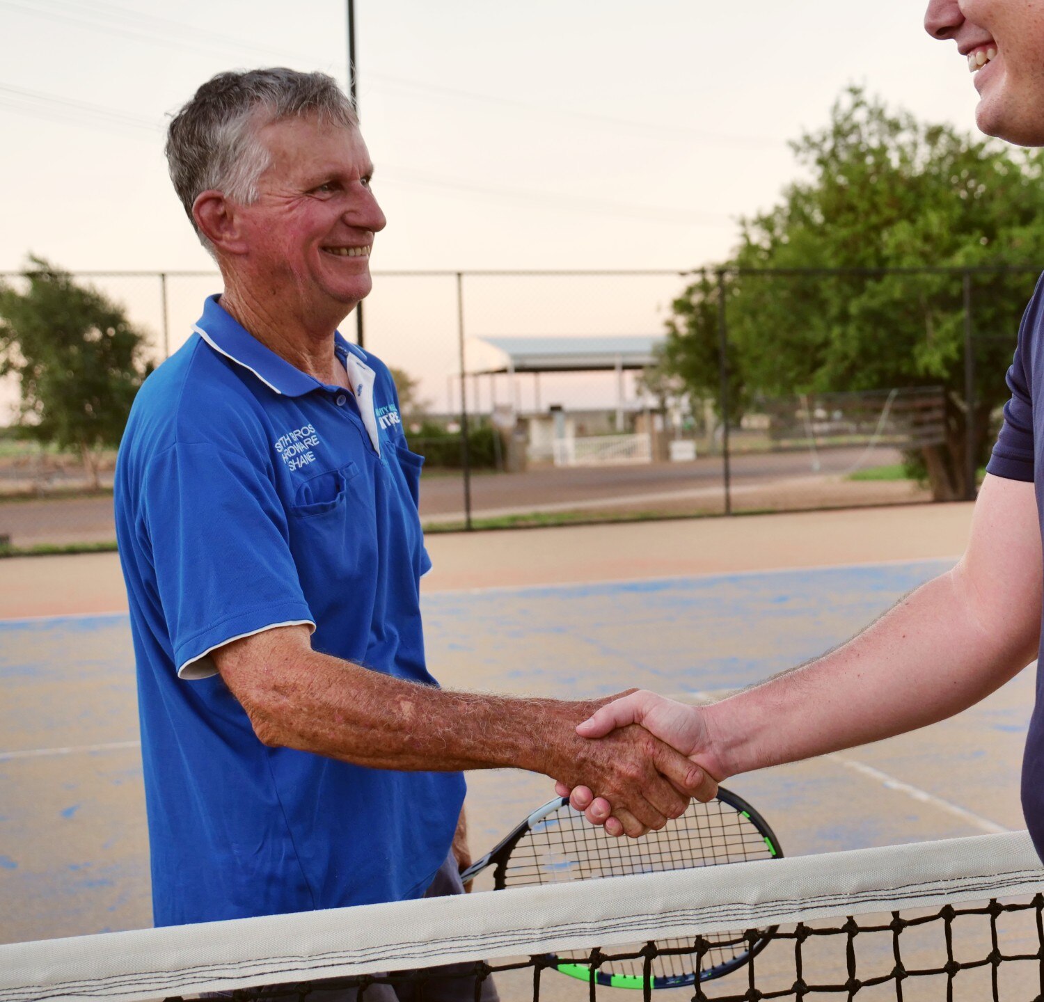 Man in blue smiling, shaking hands over net.
