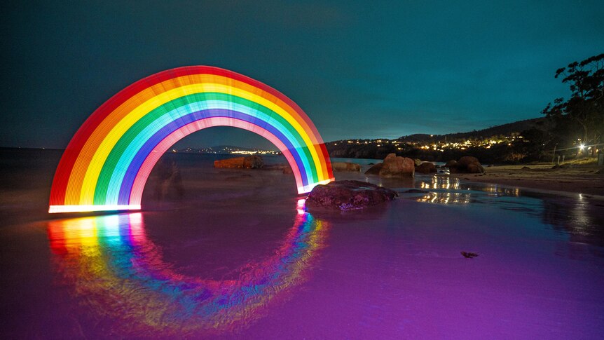 A bright rainbow created using lights in the dark on a beach in the dark.