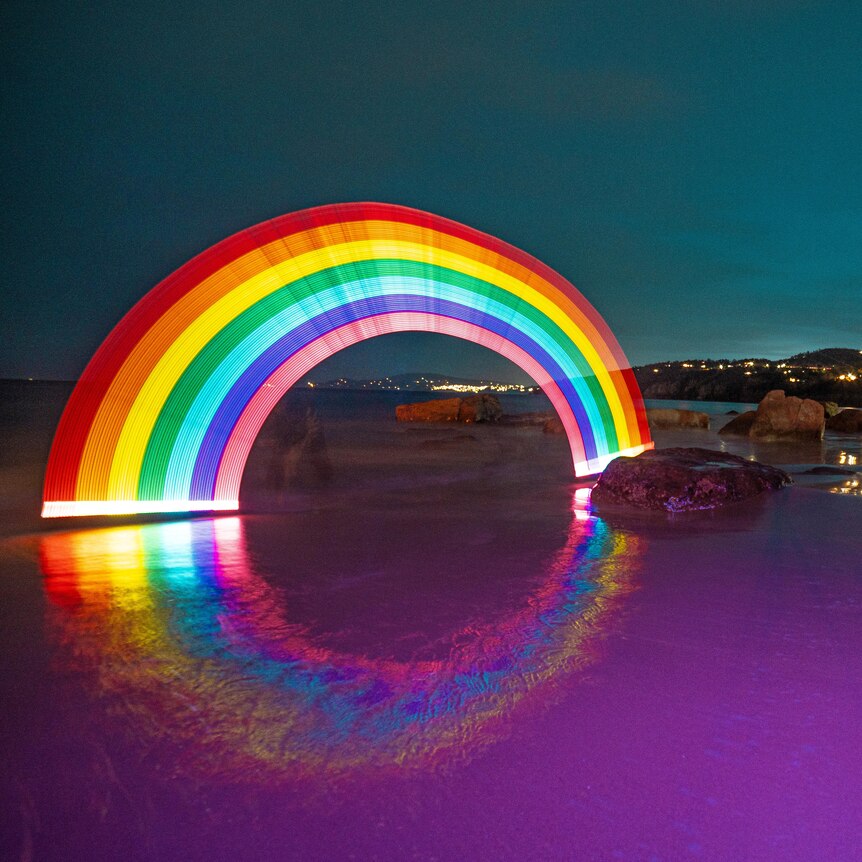 A bright rainbow created using lights in the dark on a beach in the dark.