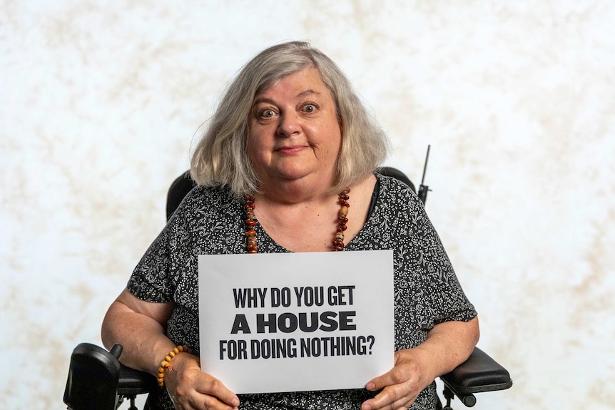Molly Taylor is holding a sign that reads "Why do you get a house for doing nothing?"