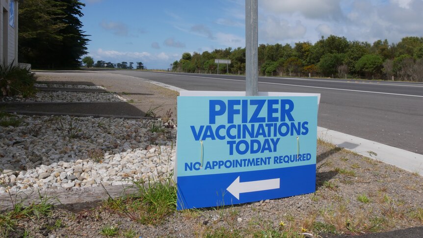 A blue sign reading 'pfizer vaccinations today' next to a highway road