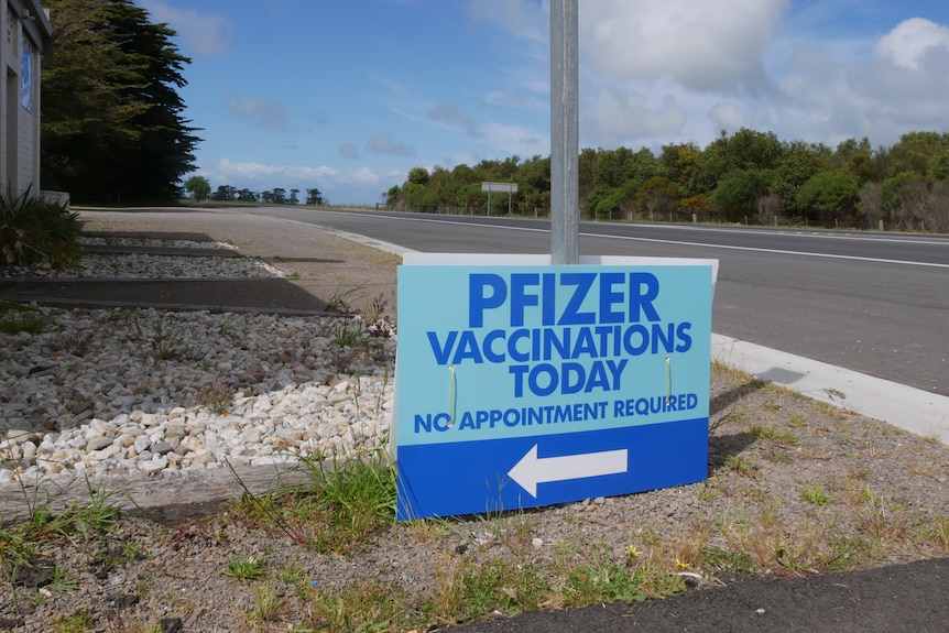 A blue sign reading 'pfizer vaccinations today' next to a highway road