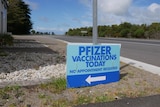 A blue sign reading 'pfizer vaccinations today' next to a highway road