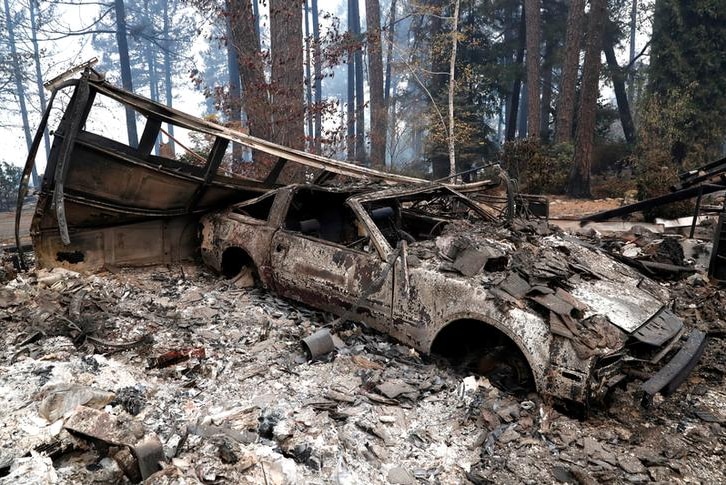 A burned out car destroyed by wildfires in Paradise, California, rests among ashes