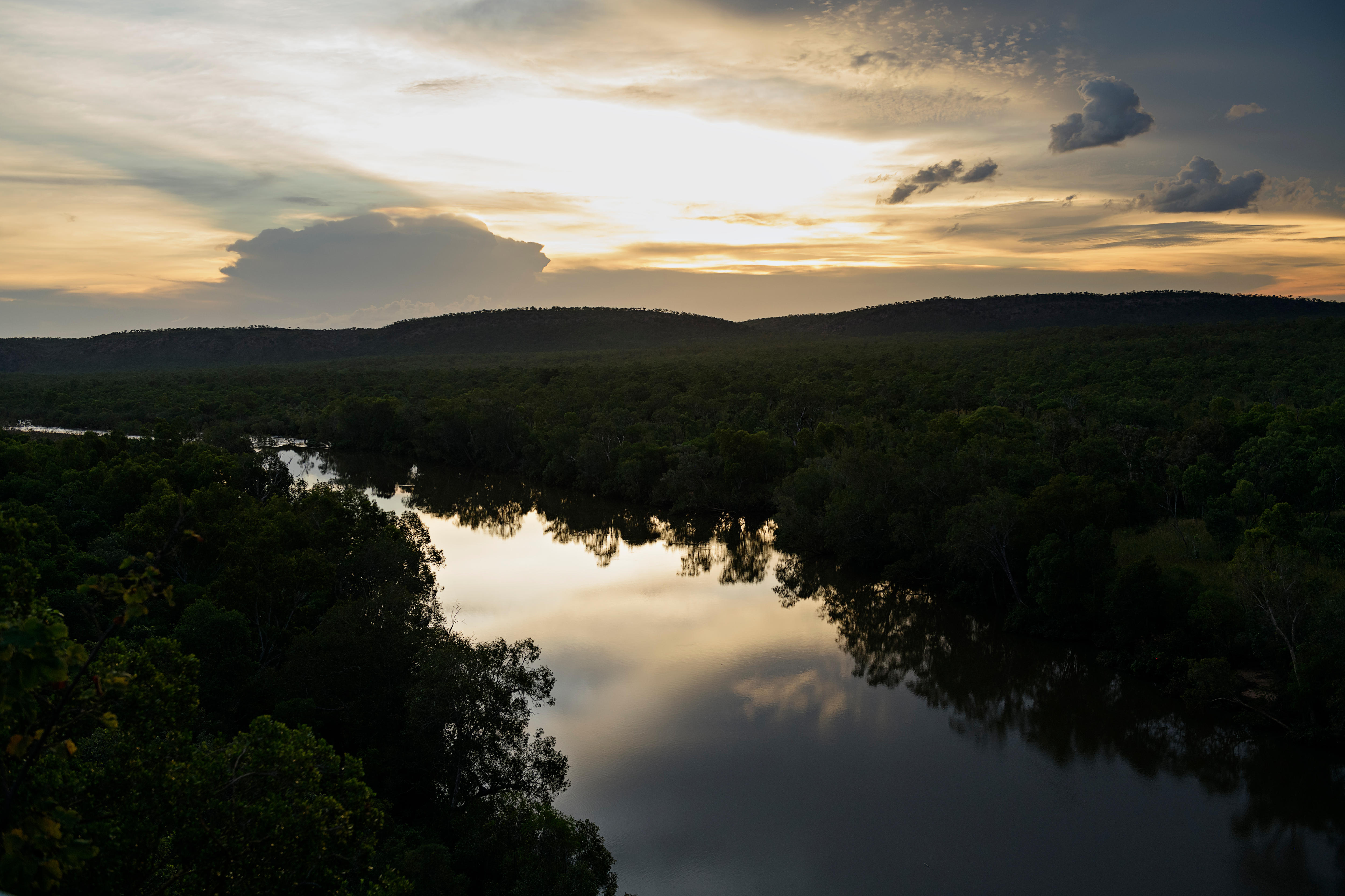 Uma imagem de uma silhueta de arbusto ao longo das margens de um rio sinuoso ao pôr do sol 
