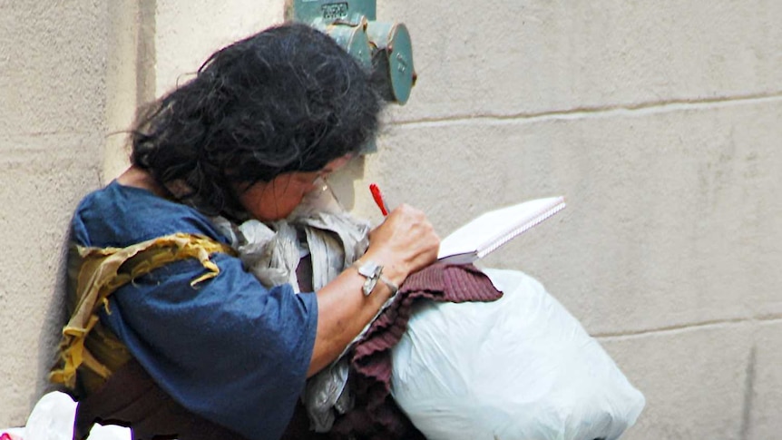 A homeless woman sits on the street with her belongings