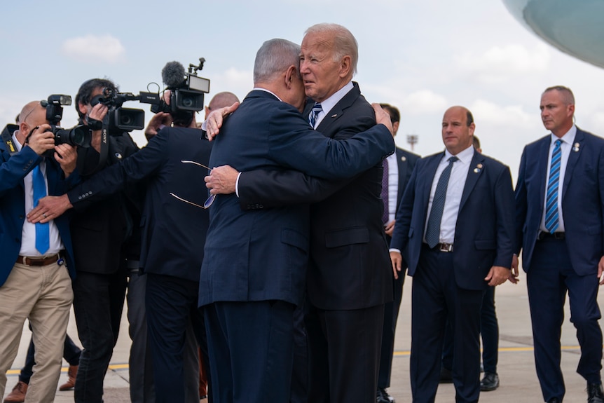 Joe Biden and Benjamin Netanyahu brace as photographers film and take pictures.