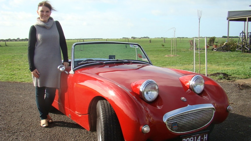 woman standing next to a red sports cars with bug eyes as head lights