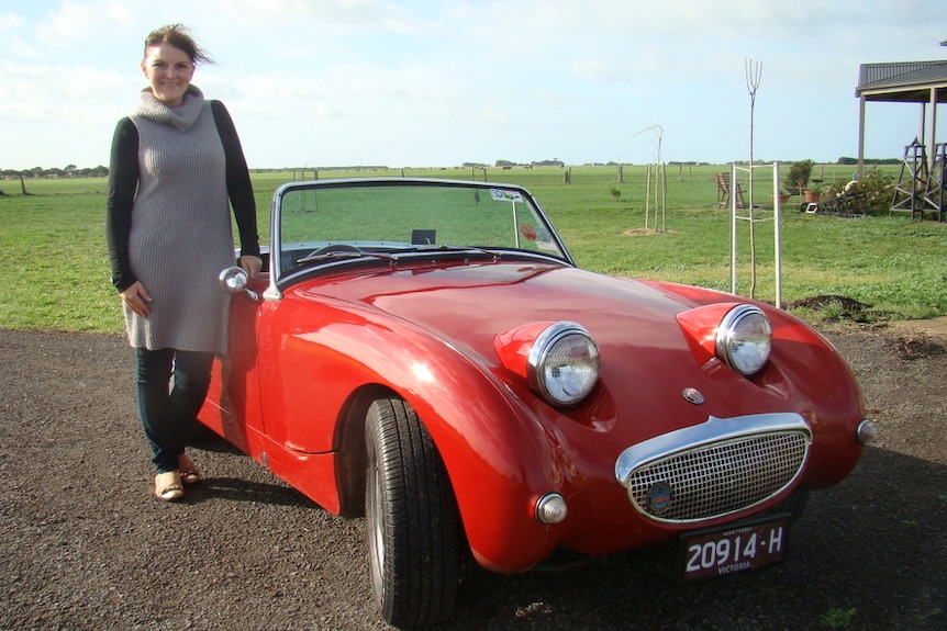 woman standing next to a red sports cars with bug eyes as head lights