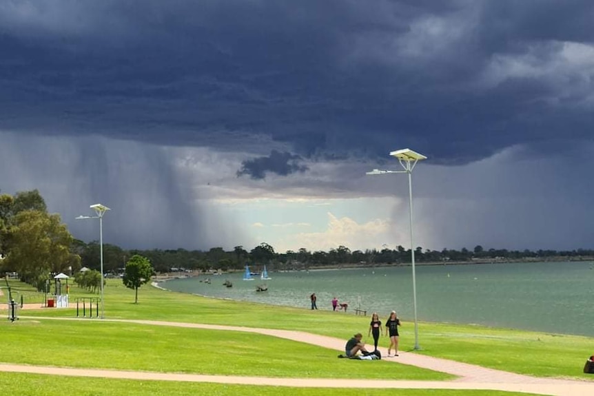 A lake with grassed areas and people walking and the sky showing an approaching storm