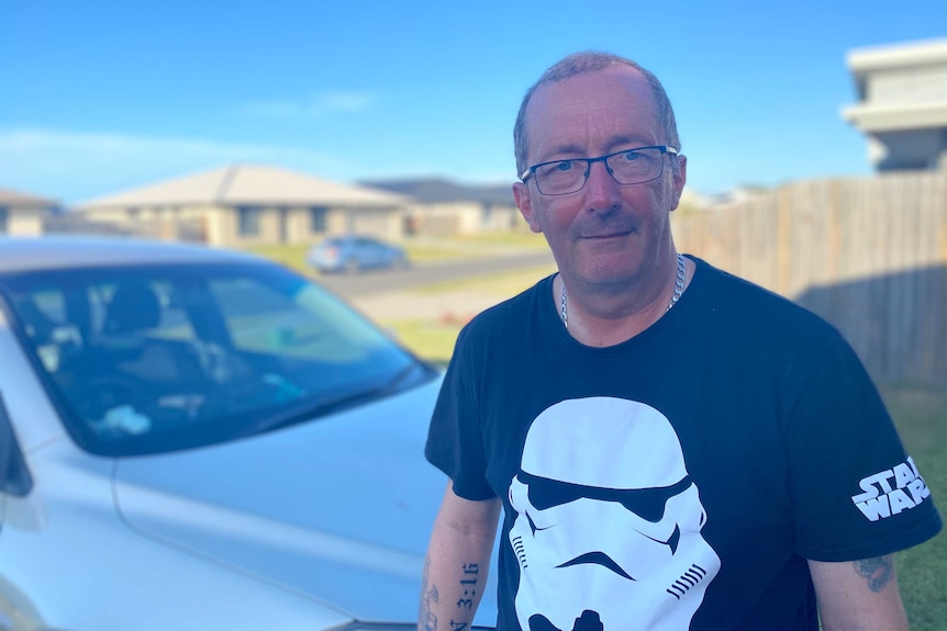 A man in a black Star Wars t-shirt stands in his driveway on a sunny day.