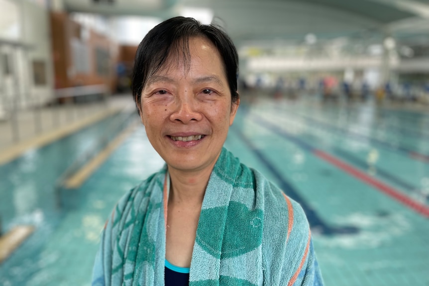 A woman in a towel smiles from outside the pool.