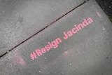 Pink graffiti painted on a cement footpath reads "#Resign Jacinda"