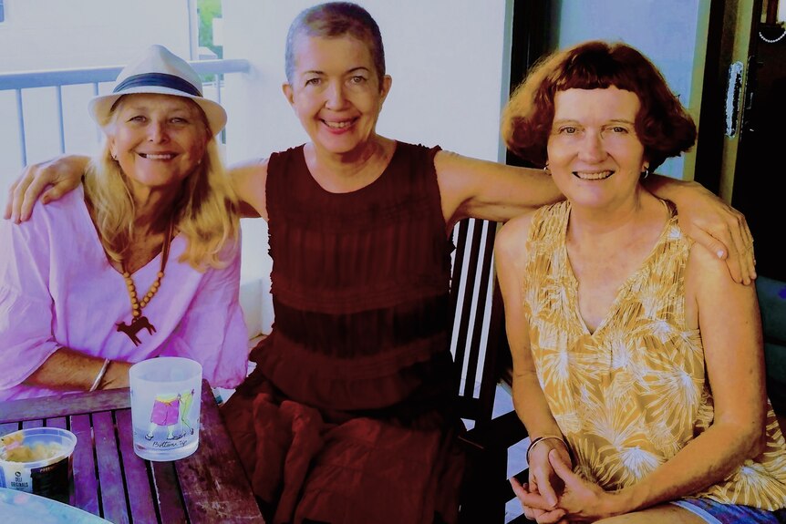 Three women, one blond, one with very short hair and one with a brown bob, smile at the camera