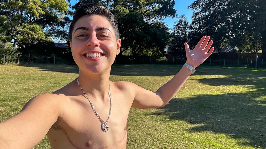 Speedy takes a shirtless selfie, their top surgery scars on show, grinning in the sunshine.