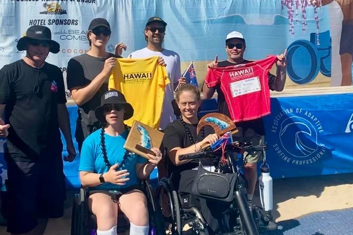 seis personas sonriendo a la cámara sosteniendo dos camisetas, dos trofeos