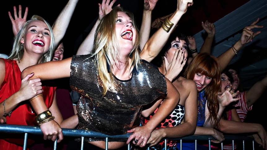 A group of women screaming and cheering in the front row of a concert.
