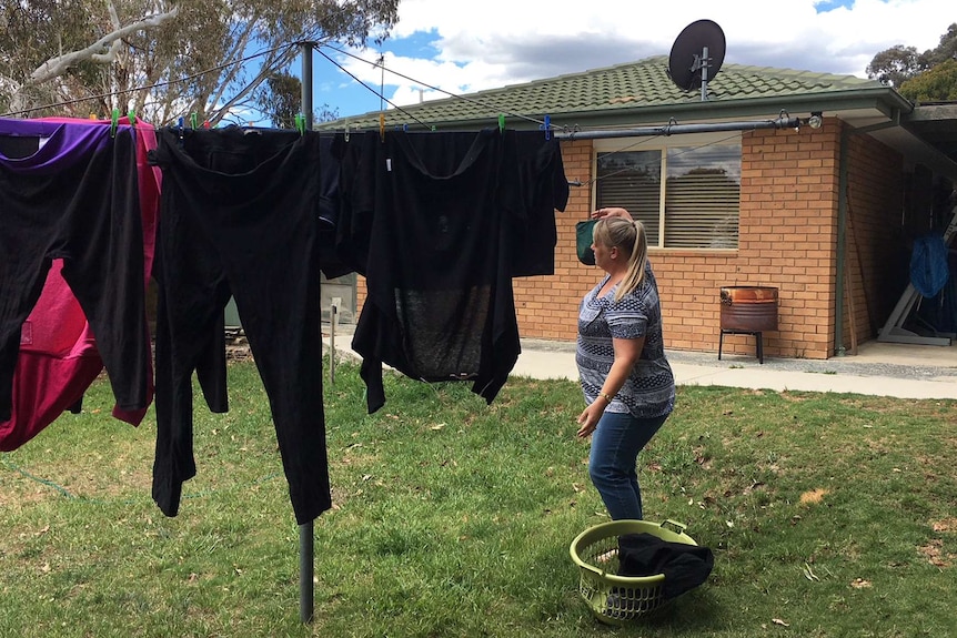 A woman hangs out washing on a clothes line in her backyard.