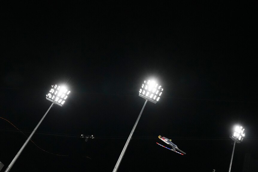 danil sadreev can be seen soaring through the air near floodlights at the winter olympics at night